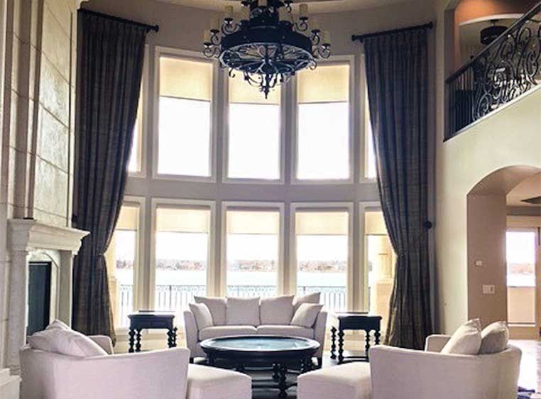 An upscale living room with a wall of tall windows with massive drapes